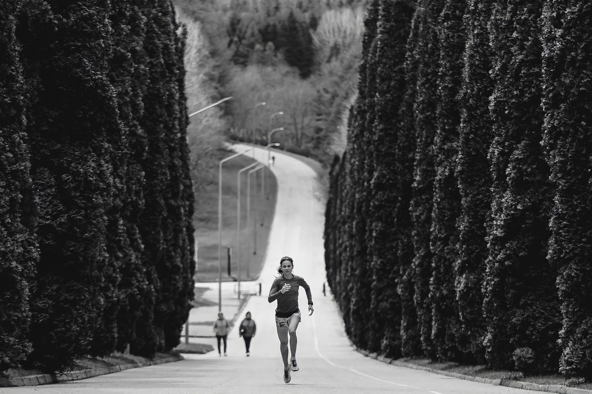 An athlete driving hard up a tree-lined road