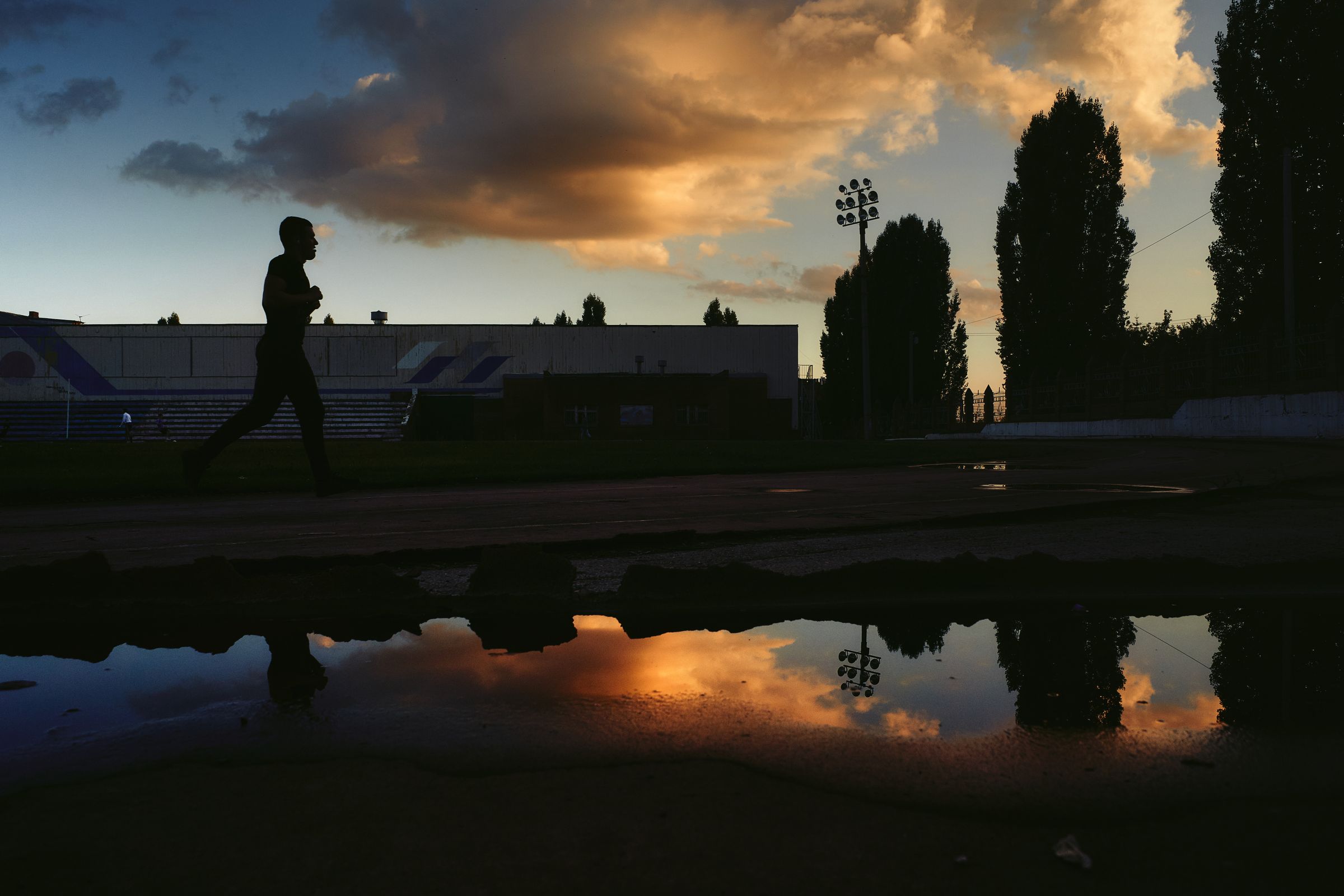A lone runner silhouetted at dusk, reflected in still water